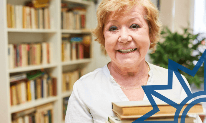 Seniorin mit Büchern Porträt einer lächelnden älteren Frau vor einem Bücherregal. Sie hält mehrere Bücher in den Händen. Rechts im Bild ist ein blaues, grafisches Sternsymbol eingeblendet.