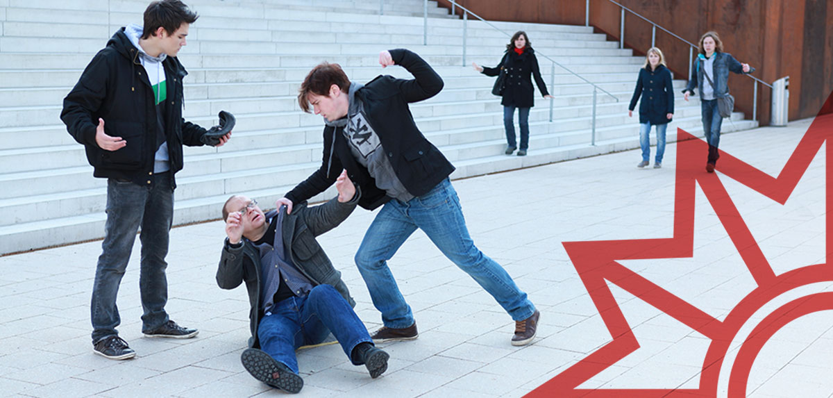 Eine Person wird in der Nähe einer Treppe von zwei Personen angegriffen, während mehrere Menschen zusehen.